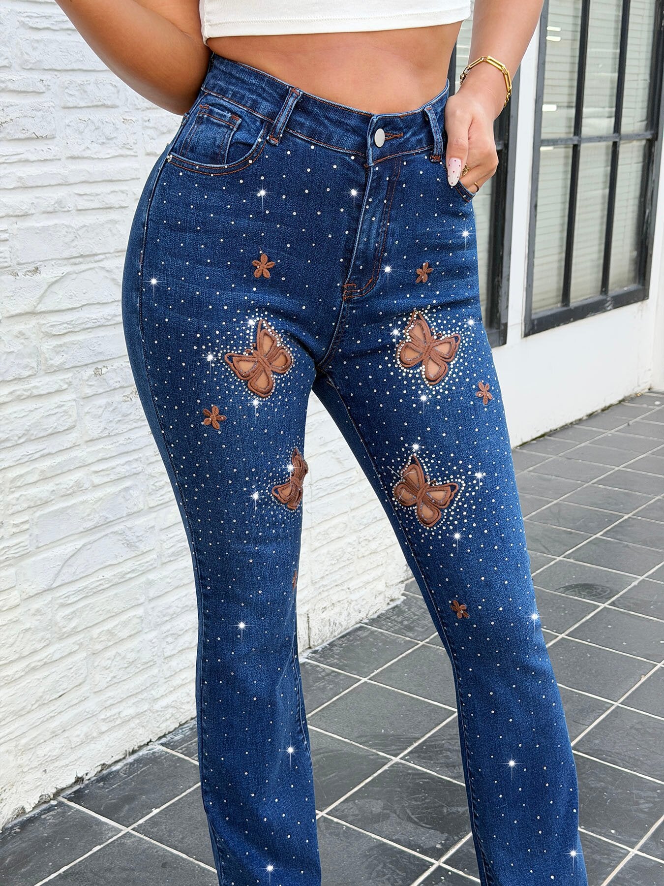 Close up of butterfly cutout rhinestone and embroidery details on party ready dark blue bootcut jeans for women – stretch denim pants decoration shot
